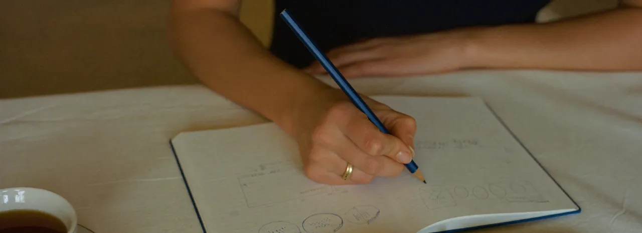 Mão a desenhar diagramas num caderno, ao lado de uma chávena de chá